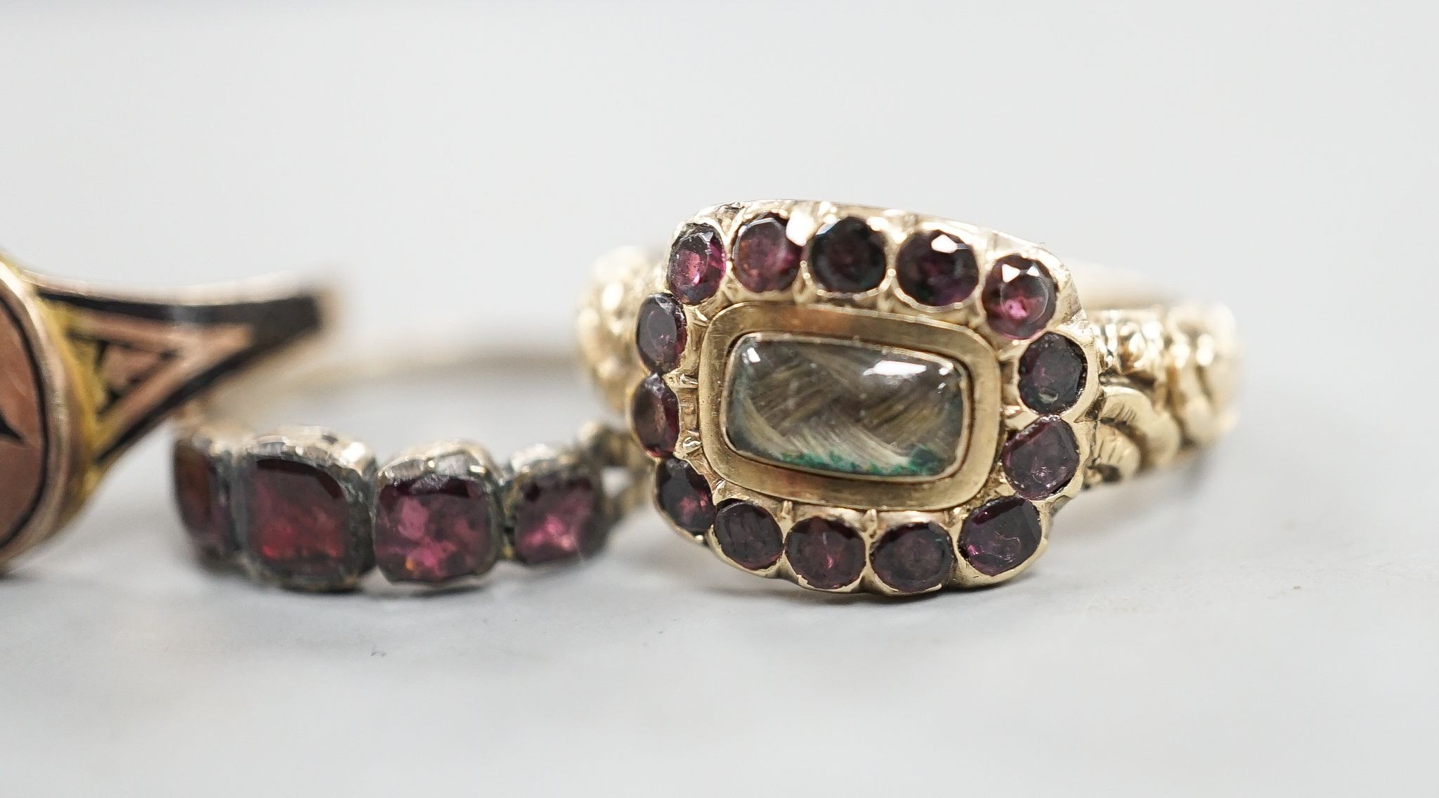 A late George III yellow metal, garnet and plaited hair mounted mourning ring, inscribed 'Ann Haycock Obt. 1 Mar. 1817 at 25, Mary Haycock ob, 26 Mar, 1817 at 15' size N/O, gross 4.6 grams and two other antique rings.